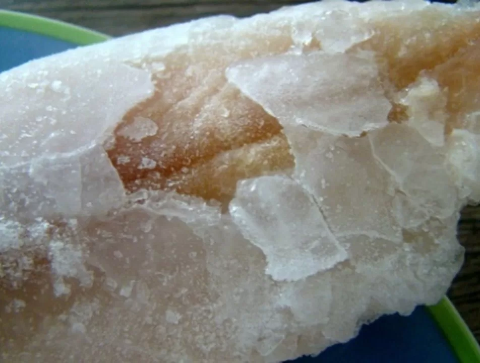 Close de um filé de peixe congelado com excesso de glaciamento, evidenciado por camadas espessas de gelo sobre a superfície do pescado.