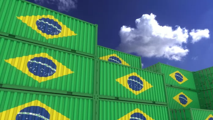 Contêineres verdes empilhados com a bandeira do Brasil estampada, sob um céu azul com nuvens.
