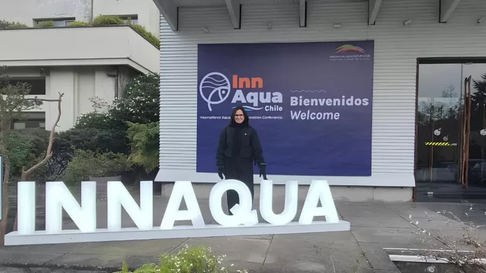Secretária Fernanda de Paula em frente ao painel do INNAQUA Chile durante o INNAQUA 2025, Puerto Varas.