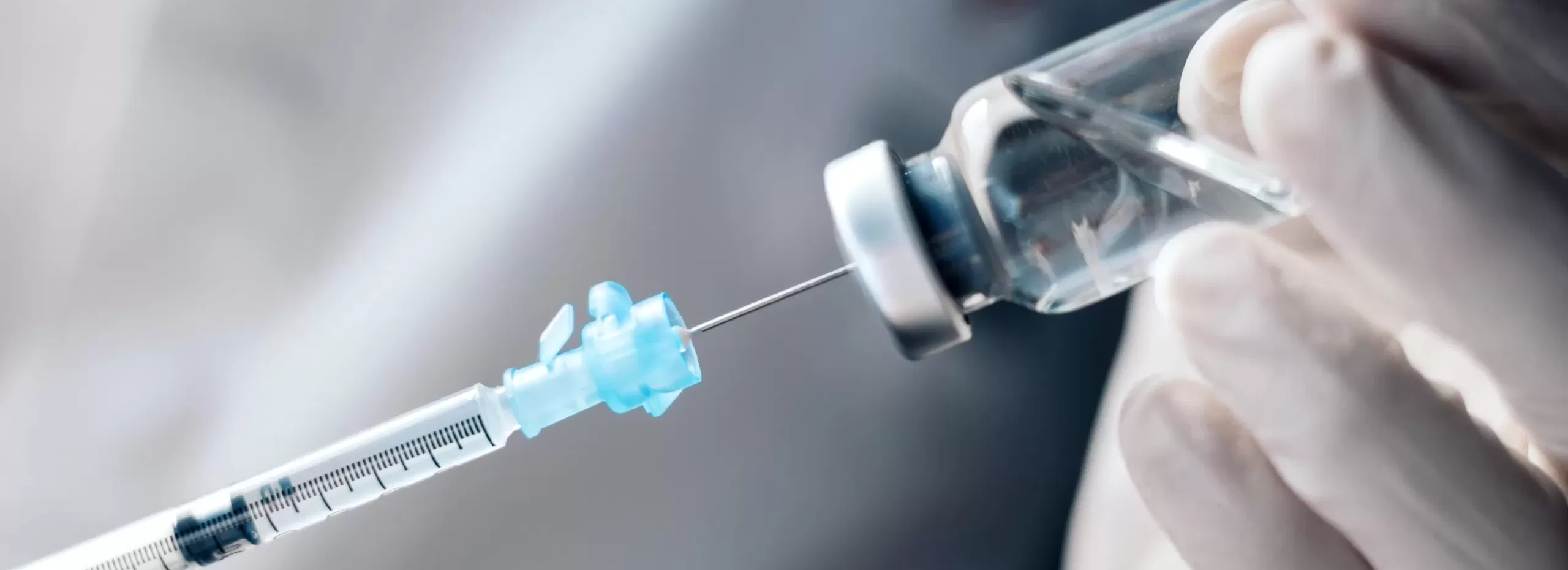Mão com luva segura frasco enquanto seringa retira dose; imagem conceitual de vacina e adjuvantes β-glucano para aquicultura.