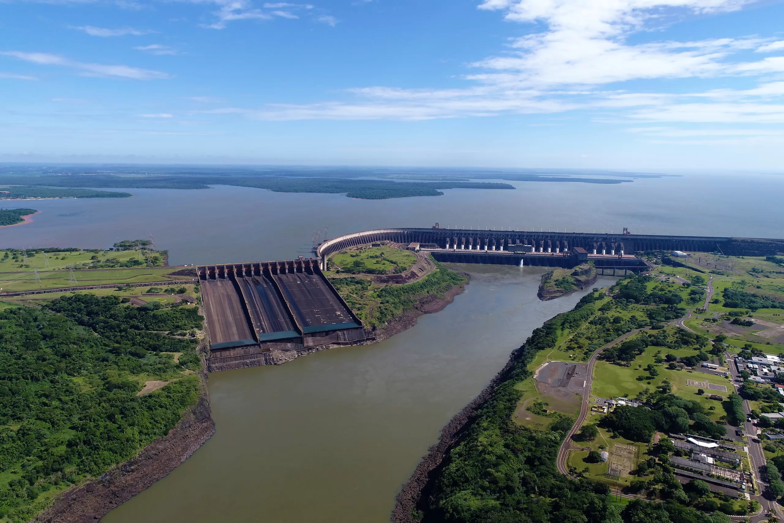 Vista aérea panorâmica da barragem da Usina Hidrelétrica de Itaipu, mostrando o vertedouro e o reservatório no Rio Paraná.