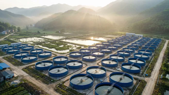 Vista aérea de sistema LBTAS com tanques circulares azuis e lagoas de tratamento retangulares cercadas por montanhas verdes.