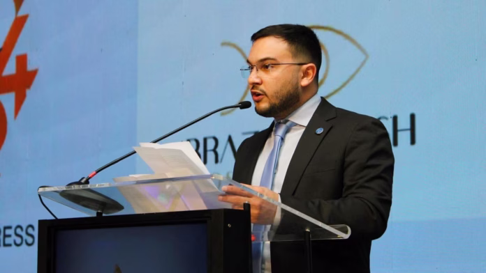 Édipo Araújo discursando em um púlpito com microfones durante evento oficial.
