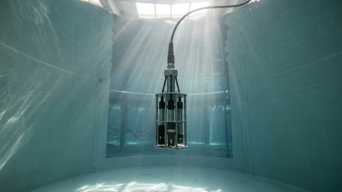 Sonda de sensor eletrônico IoT submersa em água limpa de tanque aquícola industrial para monitoramento em tempo real.
