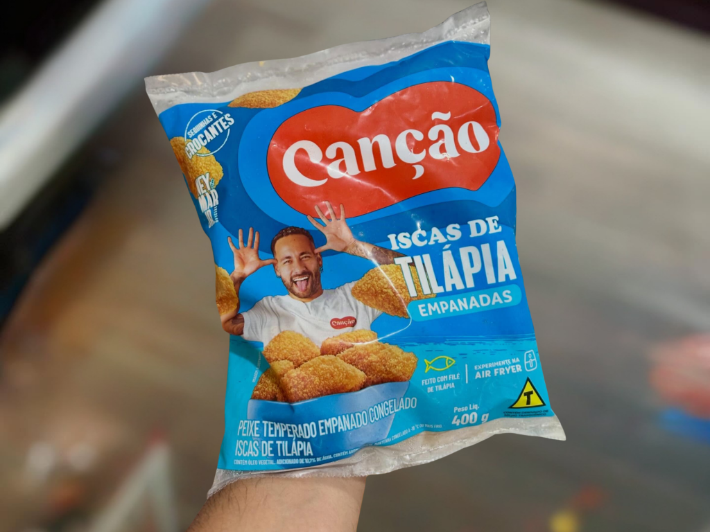 Uma mão segurando uma embalagem de produto congelado de tilápia.
